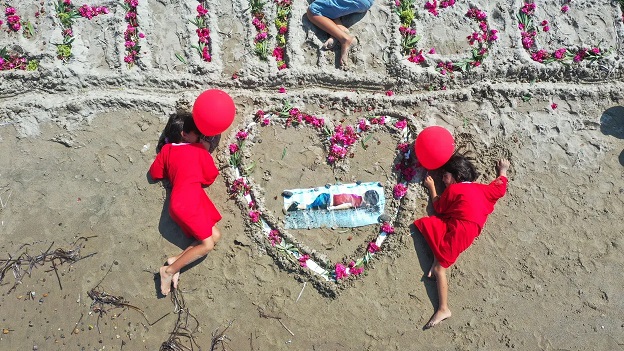 Crédits : Ali Balli/Anadolu Agency via Getty Images / Vue aérienne de personnes allongées sur le rivage comme Alan Kurdi, réfugié syrien de 3 ans, qui s’est noyé le 2 septembre 2015 et s’est échoué sur la côte méditerranéenne turque au large de Muglaâs Bodrum après le chavirement de leur bateau.